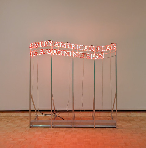 A red neon sign, all-caps, in swirling lines that suggest the stripes of a flag, reads "EVERY AMERICAN FLAG IS A WARNING SIGN".