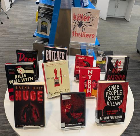 A display of books at the public library with a big label saying "Killer Thrillers" and a selection of horror titles, including "Kills Well With <something>”, “Some People Need Killing”, “The Sentence is Death”, and also “Huge” by Brent Butt.