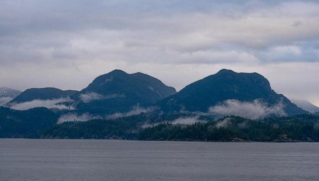 Two forested peaks, clouds nestled in the trees, across the open water.